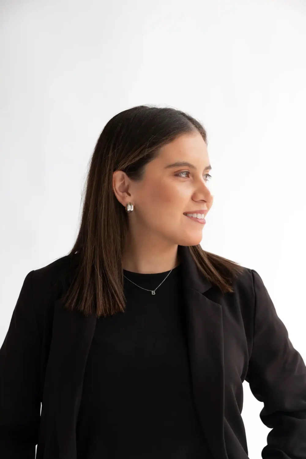 Bárbara Reyes de perfil, sonriendo, con blazer negro sobre fondo blanco de estudio