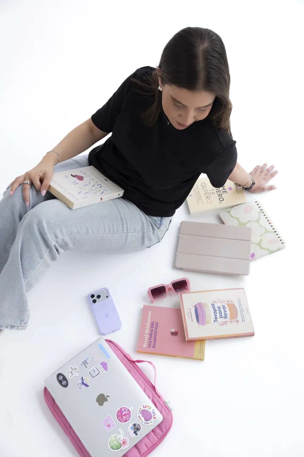 Bárbara Reyes sentada en el piso con libros de psicología, un iPad y lentes rosados